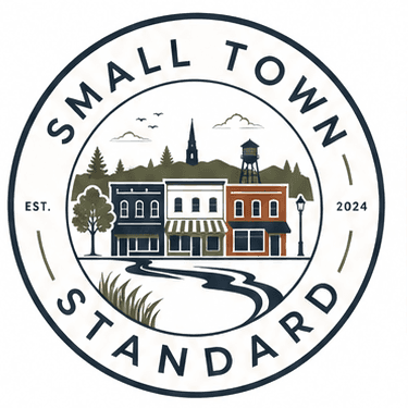 Small Town Standard seal: a main street storefront row above a river, ringed by the words Small Town Standard, established 2024.
